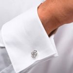 Photo of a white shirt with a close-up of a jewelled cufflink in the shape of a silver car wheel rim and a black diamond.