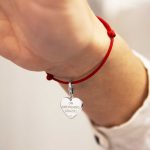 Charm a forma di cuore con scritta "Un americano, grazie!" su braccialetto rosso indossato.